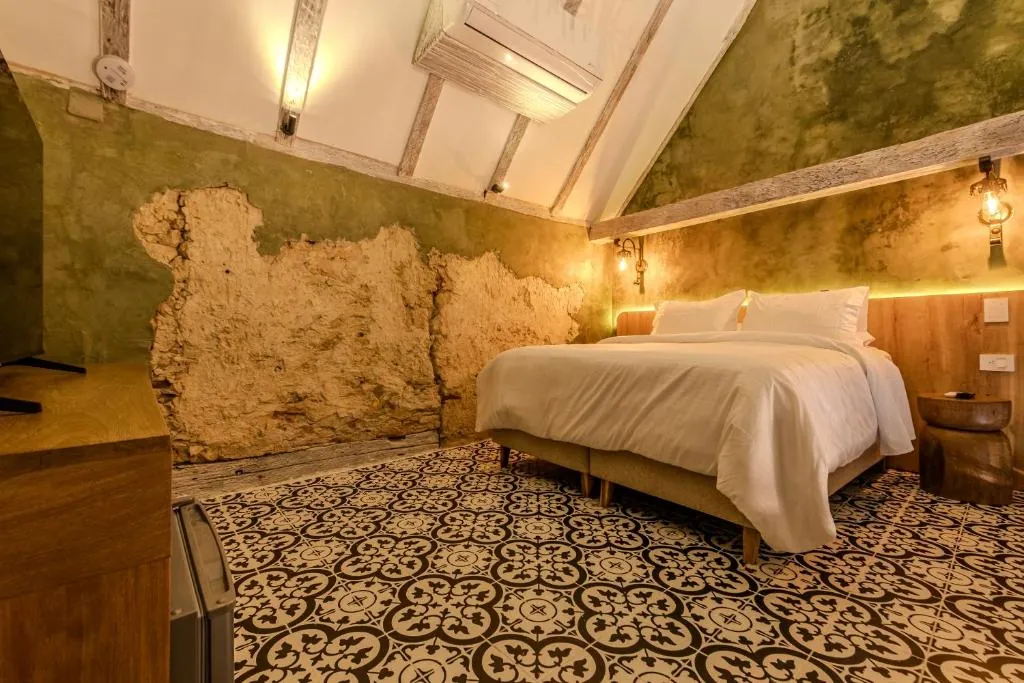 Cama de la Duplex Luxury contra un muro en verde oliva de textura original bajo techo de vigas.