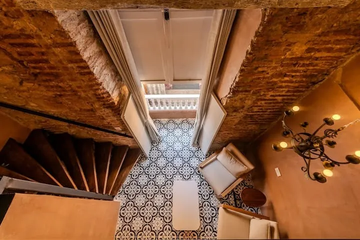 Vista desde el nivel superior de la habitación dúplex hacia la escalera de madera y el piso hidráulico.