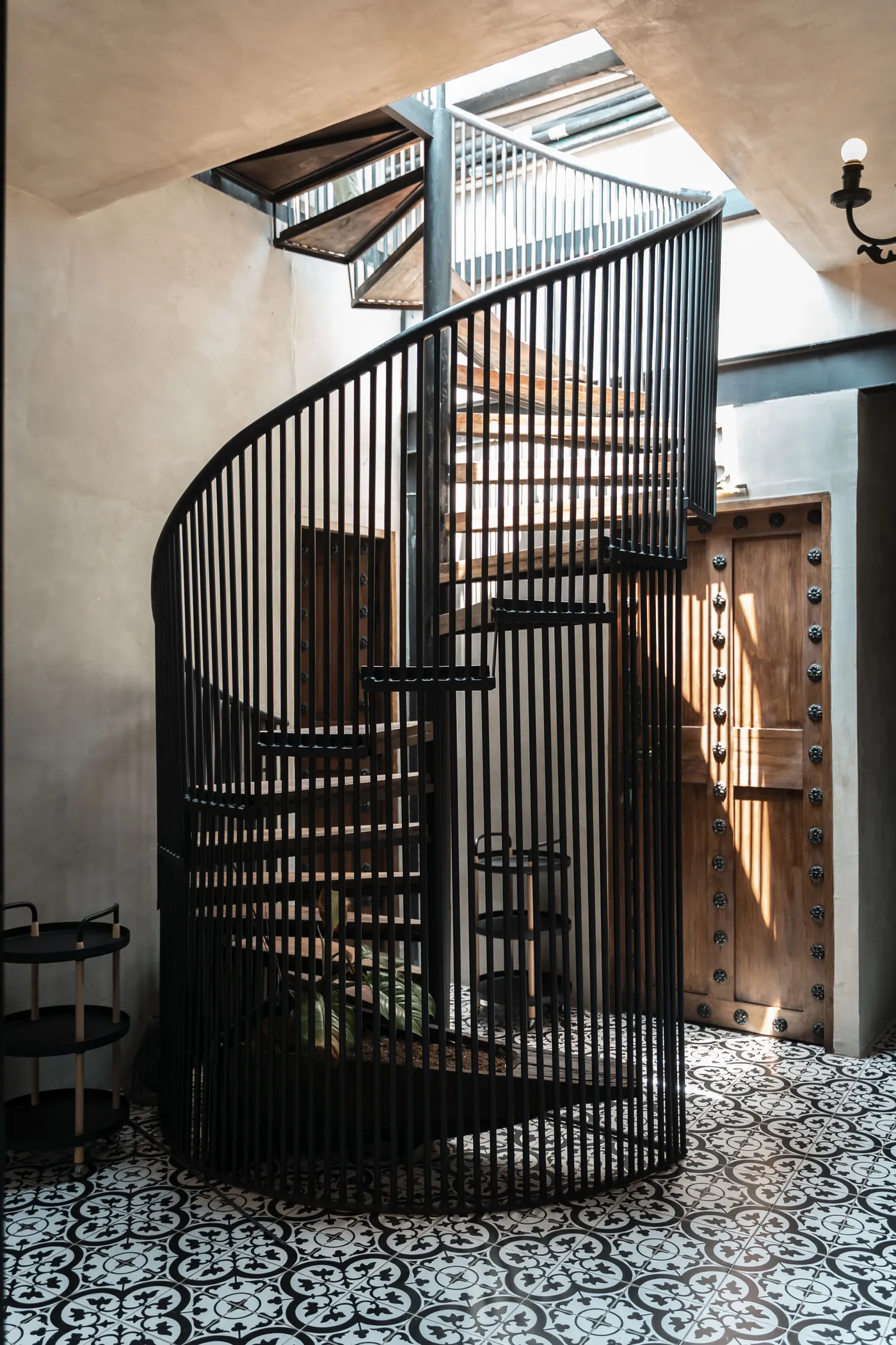 Escalera de caracol en hierro forjado que conecta los dos niveles de una suite dúplex, bajo luz cenital.