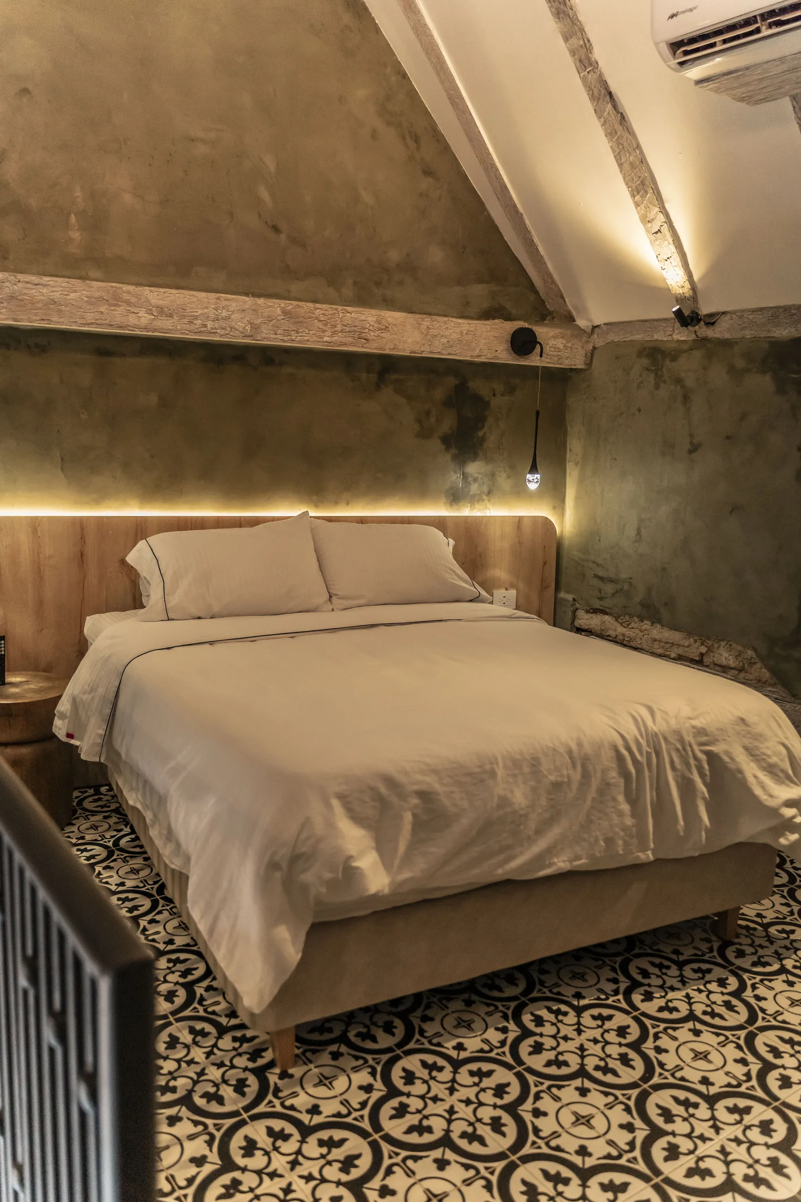 Cama de la Luxury Suite bajo el techo a dos aguas, con muro en verde oliva y luz cálida.