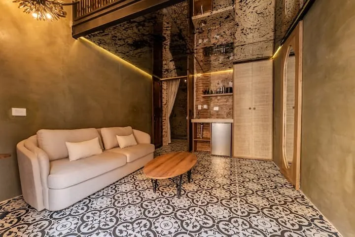 Sala de la Luxury Suite con sofá crema, muro en verde oliva y piso de baldosa hidráulica.